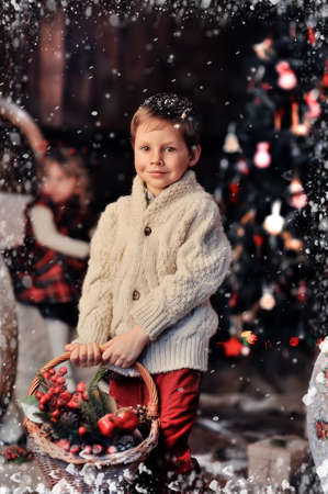 boy stands with a basket of toys in the background of a beautiful Christmas treeの写真素材