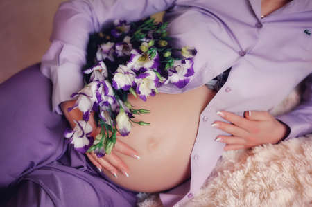 close-up of pregnant woman s belly in a purple dress with beautiful flowers