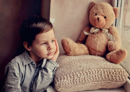 little boy with a toy on a knitted pillow looking out the windowの写真素材