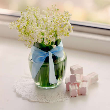 vase on a white napkin with a blue ribbon and a bouquet of lilies of the valleyの写真素材