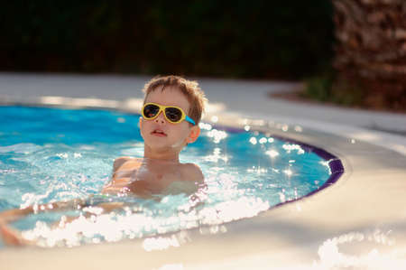 hot sunny day, the boy with sunglasses floating in the poolの写真素材