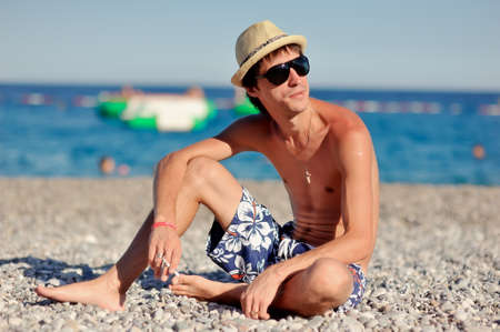 young man in sunglasses and a straw hat sitting on the beachの写真素材
