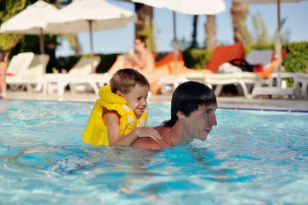 hot day a little boy in a yellow life jacket and dad swimming in the poolの写真素材