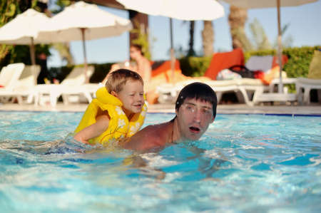 hot day a little boy in a yellow life jacket and dad swimming in the poolの写真素材