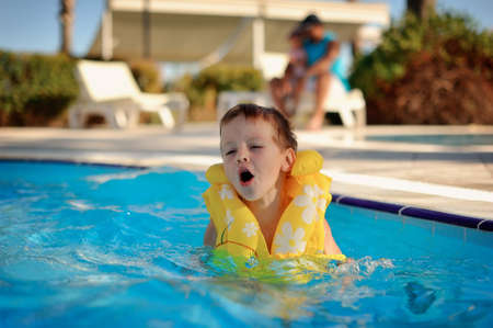 hot day a little boy in a yellow life jacket floating in the poolの写真素材