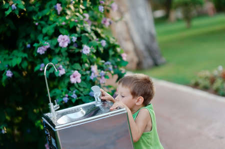 little boy reaching for the tap water in the street to get a drink of waterの写真素材