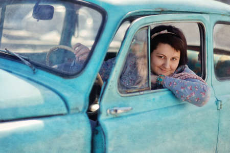 beautiful girl sitting in an old car and smiling with pleasureの写真素材