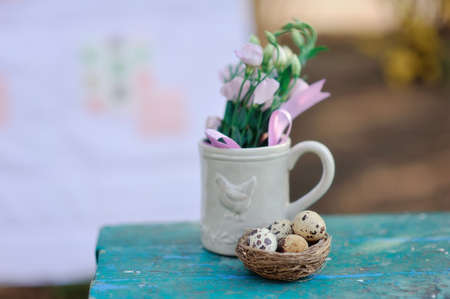 quail eggs in the nest and a cup with flowers on a blue bench