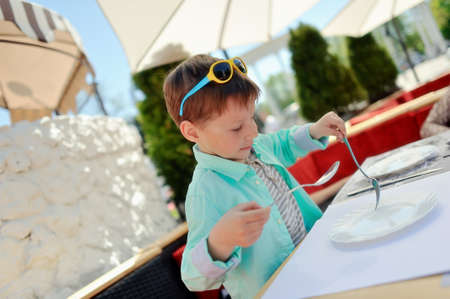 stylish little boy with sunglasses sitting at a table in a restaurantの写真素材