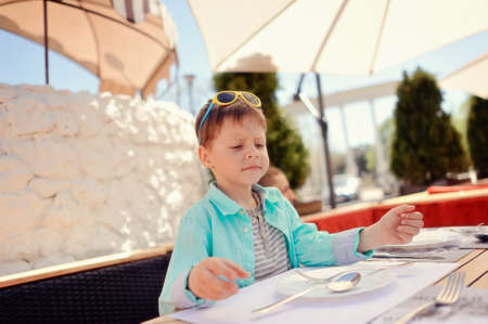 stylish little boy with sunglasses sitting at a table in a restaurantの写真素材
