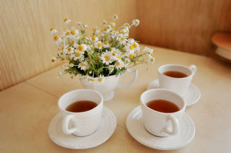 beautiful table setting of white cups of tea and white vase bouquet of daisiesの写真素材
