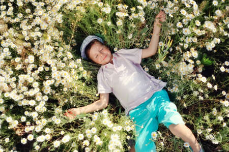 on a meadow boy in blue shorts and a cap is in daisiesの写真素材