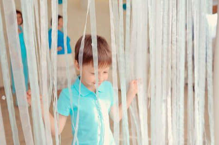 little boy in blue jacket posing behind a transparent curtainの写真素材