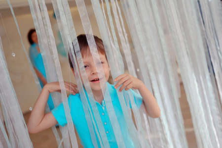 little boy in blue jacket posing behind a transparent curtainの写真素材