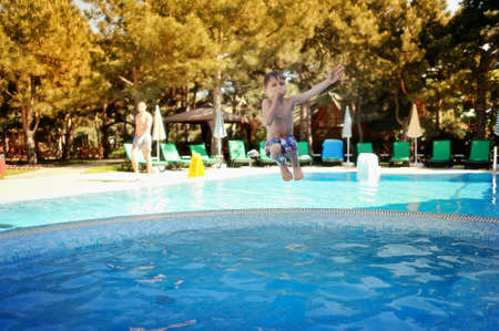 little boy jumping a hot summer day in a blue swimming poolの写真素材
