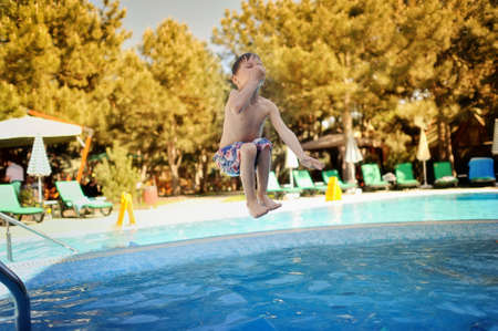 little boy jumping a hot summer day in a blue swimming poolの写真素材