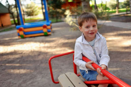 cheerful handsome boy in a white jacket swinging on a swingの写真素材
