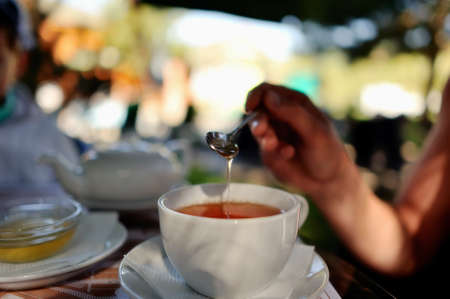 close-up of white cup of tea and honey dripping from a spoon into the teaの写真素材