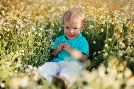 on the nature of the little baby playing and smiling on a field strewn with wild daisiesの写真素材
