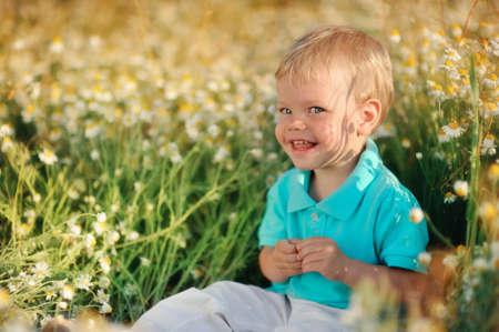 on the nature of the little baby playing and smiling on a field strewn with wild daisiesの写真素材