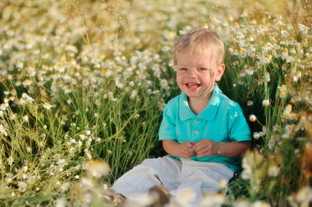 on the nature of the little baby playing and smiling on a field strewn with wild daisiesの写真素材