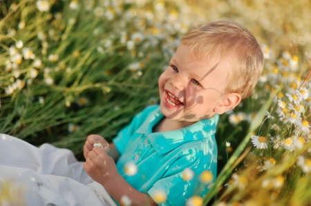 on the nature of the little baby playing and smiling on a field strewn with wild daisiesの写真素材
