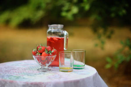 on a white table is a jar of strawberry compote and glasses and a bowl of strawberriesの写真素材