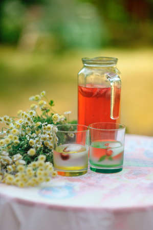 on a white table is a jar of strawberry compote and glasses and a bouquet of daisiesの写真素材