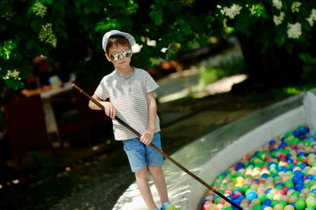little boy in a cap and sunglasses collects a net colored ballsの写真素材