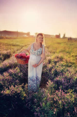 at sunset walks on the field a pregnant woman with a basket of flowersの写真素材