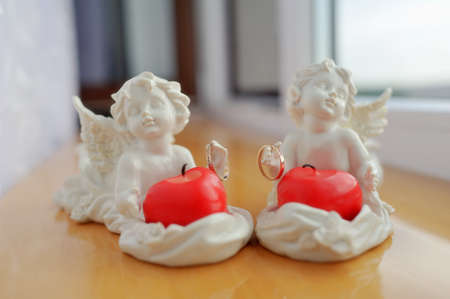 two white angel with red candles holding wedding ringsの写真素材