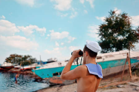 on the shore at the pier on the sea background young man in the Marine dress and a pair of...