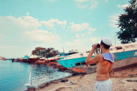 on the shore at the pier on the sea background young man in the Marine dress and a pair of binocularsの写真素材