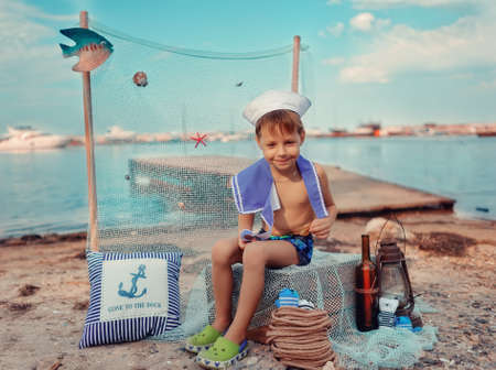 on the shore at the pier on the sea background sits a boy in the Marine dressの写真素材