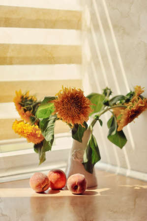 on the table in the sun is a vase with yellow flowers and scattered peachの写真素材