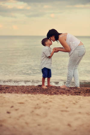 mother and son walking barefoot on the beach at sunsetの写真素材