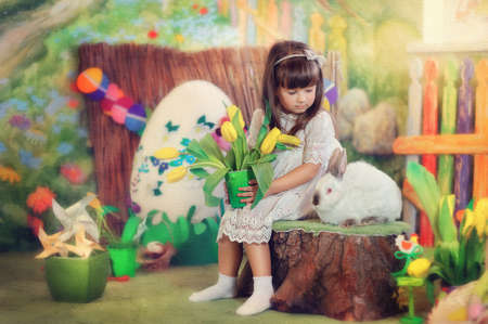 Easter composition of a little girl in a white dress with a rabbit and flowersの写真素材