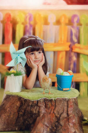 cute little girl in a white dress sitting with a chicken on a tree stumpの写真素材