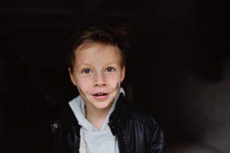 portrait of a mischievous boy with a dirty face in a black jacketの写真素材