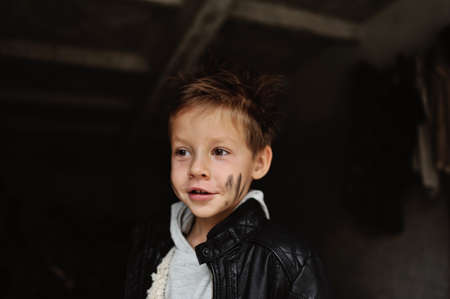 portrait of a mischievous boy with a dirty face in a black jacketの写真素材