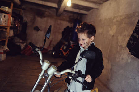in the garage of a boy with dirty face and stylish hairstyle repairs mopedの写真素材