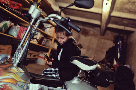 in the garage of a boy with dirty face and stylish hairstyle repairs mopedの写真素材