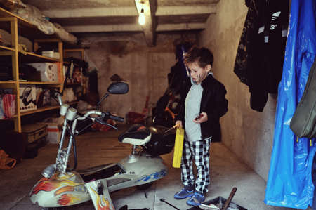 in the garage of a boy with dirty face and stylish hairstyle repairs mopedの写真素材