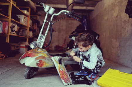 in the garage of a boy with dirty face and stylish hairstyle repairs mopedの写真素材