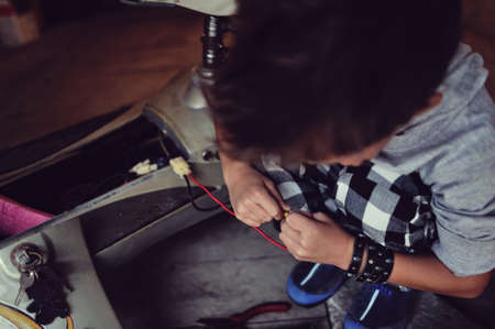 in the garage of a boy with dirty face and stylish hairstyle repairs mopedの写真素材