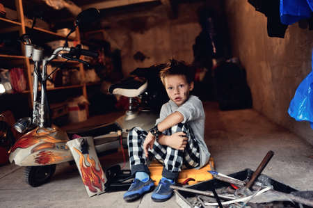in the garage of a boy with dirty face and stylish hairstyle repairs mopedの写真素材