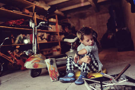 in the garage of a boy with dirty face and stylish hairstyle repairs mopedの写真素材