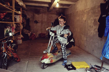 in the garage of a boy with dirty face and stylish hairstyle on a mopedの写真素材