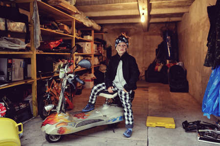 in the garage of a boy in a black jacket with a dirty face on a mopedの写真素材