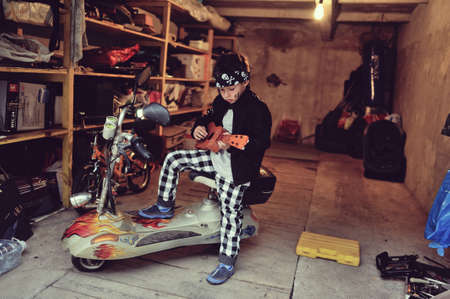 in the garage of a boy with dirty face and a moped with a guitarの写真素材